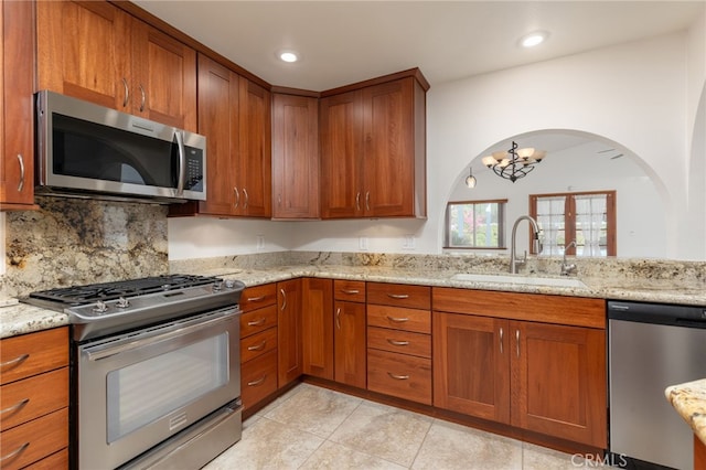 kitchen with light stone countertops, appliances with stainless steel finishes, an inviting chandelier, and sink