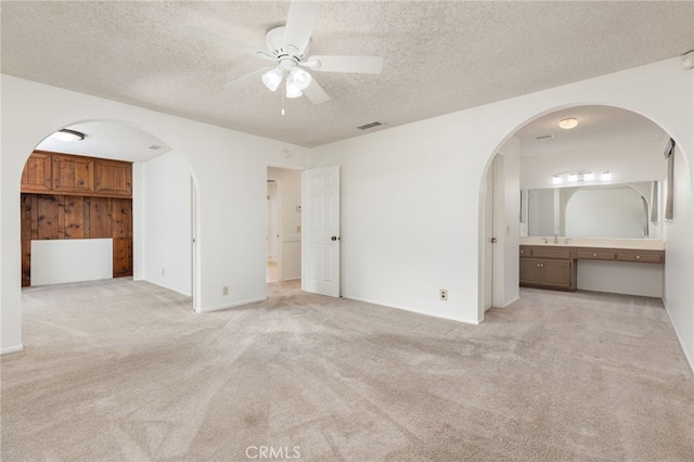 unfurnished bedroom with ensuite bathroom, ceiling fan, a textured ceiling, and light carpet