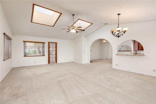 unfurnished living room featuring vaulted ceiling with skylight, ceiling fan with notable chandelier, and light colored carpet