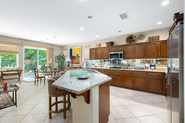 kitchen with light tile patterned flooring, sink, a kitchen bar, a kitchen island with sink, and light stone counters