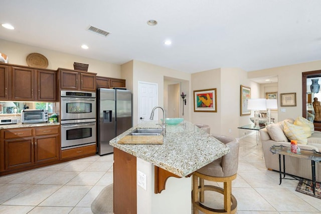 kitchen featuring an island with sink, sink, a kitchen bar, light stone counters, and stainless steel appliances