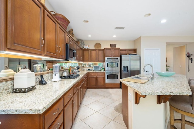 kitchen featuring sink, light tile patterned floors, a breakfast bar area, stainless steel appliances, and a center island with sink