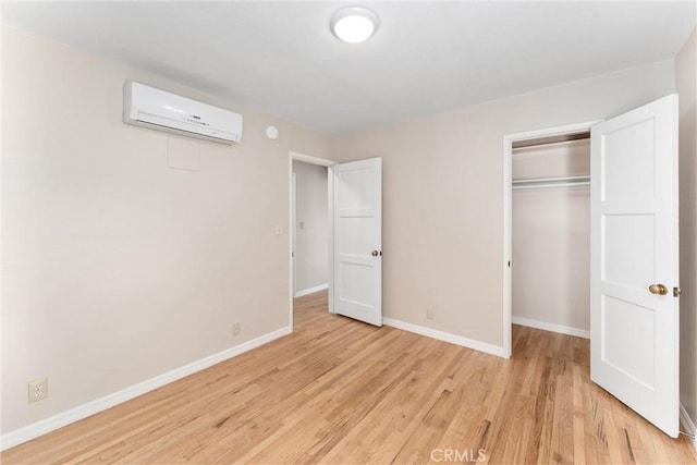 unfurnished bedroom featuring a wall unit AC, a closet, and light wood-type flooring