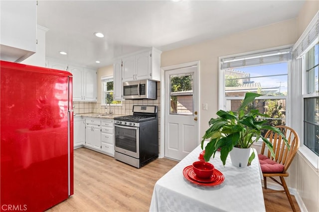 kitchen with appliances with stainless steel finishes, light wood-type flooring, backsplash, sink, and white cabinetry