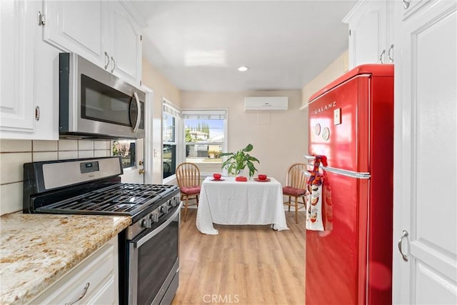 kitchen featuring light hardwood / wood-style flooring, decorative backsplash, appliances with stainless steel finishes, a wall mounted AC, and white cabinetry