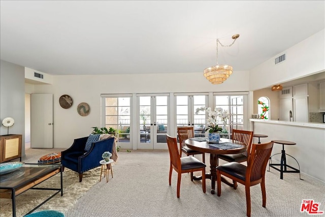 carpeted dining space featuring french doors, plenty of natural light, and a notable chandelier