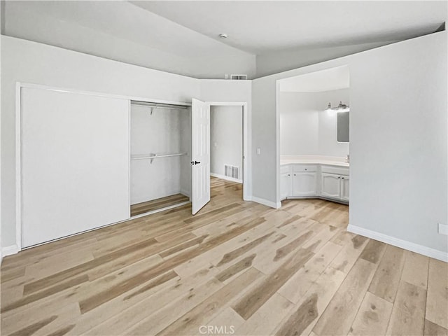 unfurnished bedroom featuring light hardwood / wood-style flooring, ensuite bath, a closet, and lofted ceiling