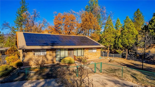 view of front of house with brick siding, fence, and roof mounted solar panels