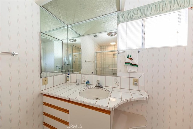 bathroom with visible vents, a tile shower, vanity, and wallpapered walls