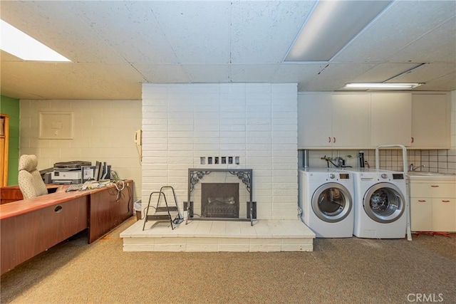 washroom featuring concrete block wall, cabinet space, a brick fireplace, a sink, and separate washer and dryer