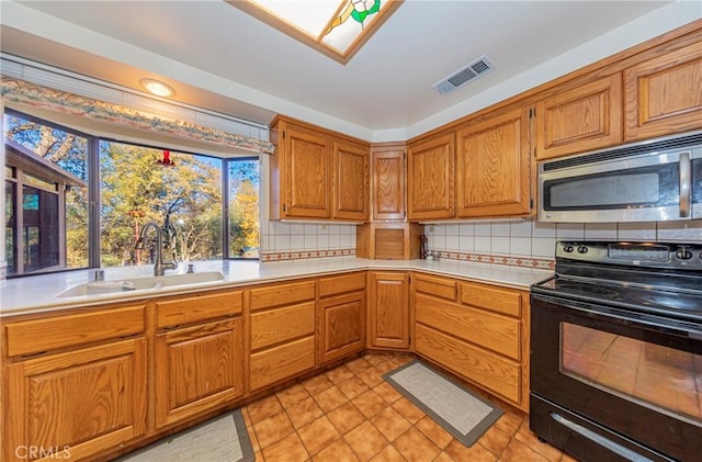 kitchen featuring visible vents, stainless steel microwave, light countertops, black range with electric cooktop, and a sink