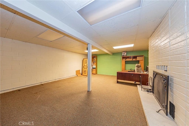 finished below grade area featuring concrete block wall, a fireplace, and a paneled ceiling