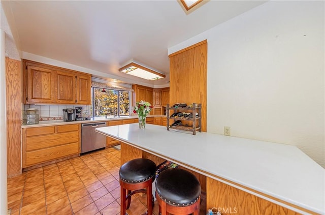 kitchen featuring light tile patterned floors, tasteful backsplash, light countertops, dishwasher, and a peninsula