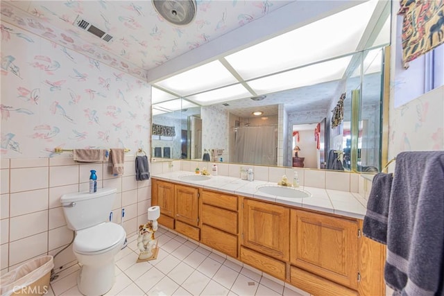 full bath featuring wallpapered walls, a shower stall, a sink, and wainscoting