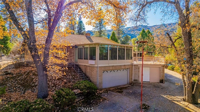 back of property with concrete driveway, a sunroom, a chimney, stairway, and an attached garage