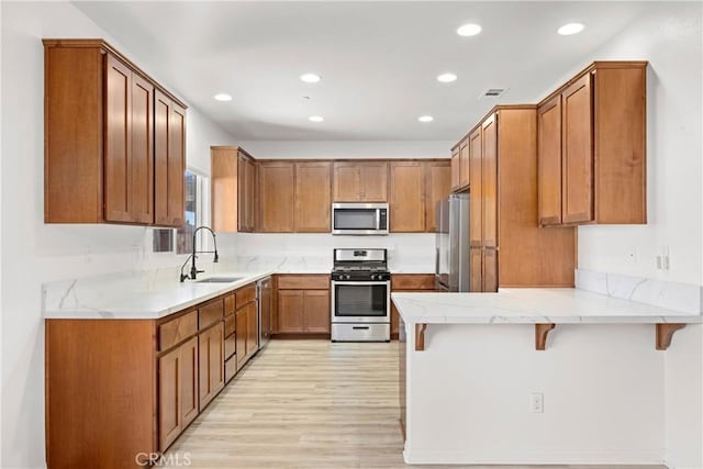 kitchen featuring kitchen peninsula, appliances with stainless steel finishes, light hardwood / wood-style flooring, a breakfast bar, and sink