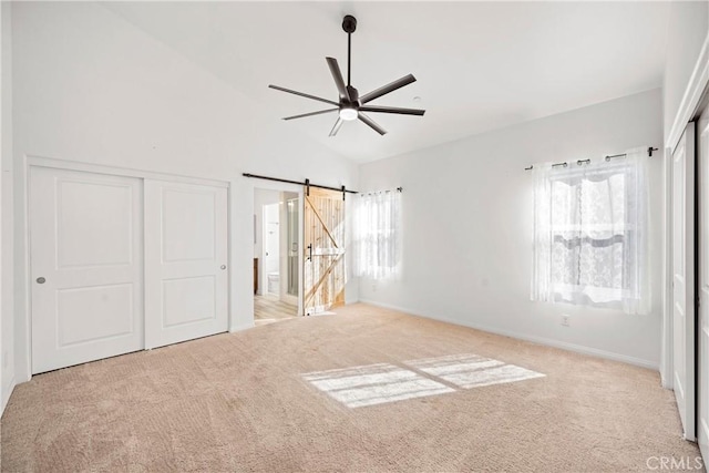 unfurnished bedroom with light carpet, a barn door, ceiling fan, a closet, and vaulted ceiling