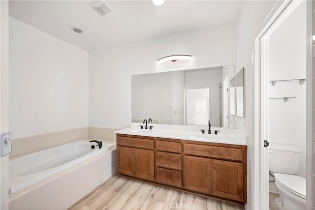 bathroom featuring toilet, tiled bath, hardwood / wood-style floors, and vanity