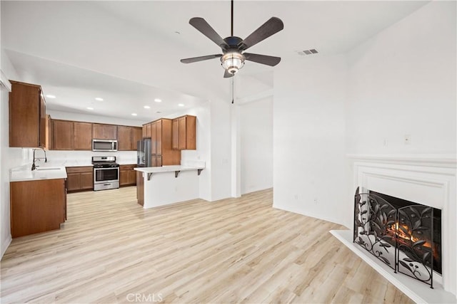 kitchen with light hardwood / wood-style floors, ceiling fan, stainless steel appliances, a breakfast bar, and sink