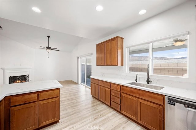 kitchen featuring lofted ceiling, light hardwood / wood-style floors, stainless steel dishwasher, sink, and light stone countertops