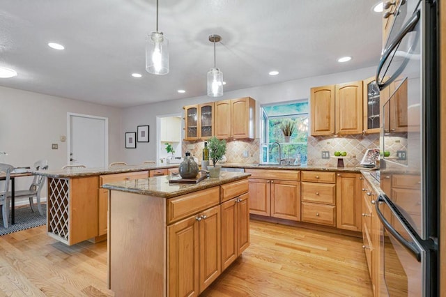 kitchen featuring a kitchen island, stainless steel refrigerator, sink, hanging light fixtures, and light hardwood / wood-style floors