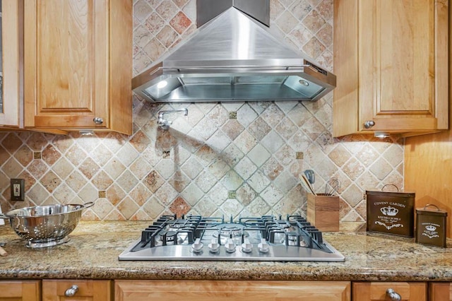 kitchen with light stone counters, wall chimney range hood, decorative backsplash, and stainless steel gas stovetop