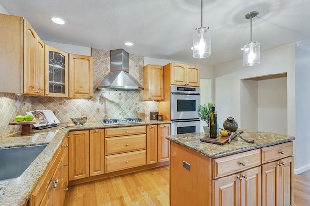 kitchen with wall chimney exhaust hood, pendant lighting, stainless steel appliances, light stone countertops, and light hardwood / wood-style floors