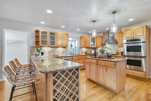 kitchen featuring a kitchen island, pendant lighting, a kitchen bar, stainless steel appliances, and wall chimney exhaust hood