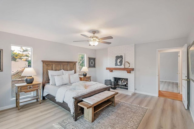 bedroom featuring multiple windows, light wood-type flooring, a fireplace, and ceiling fan