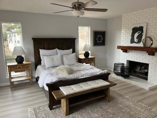 bedroom with a fireplace, ceiling fan, and light wood-type flooring