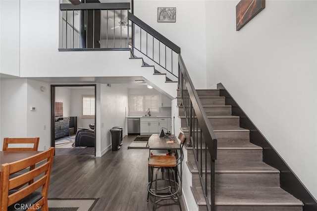 stairs with ceiling fan, hardwood / wood-style floors, a towering ceiling, and sink