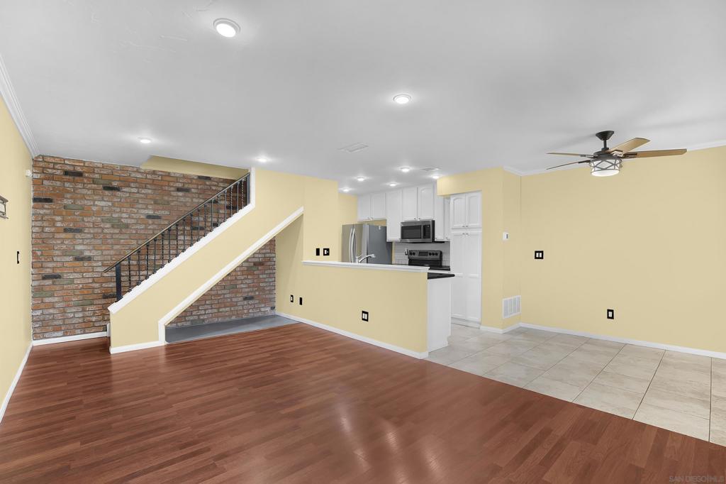 unfurnished living room featuring light hardwood / wood-style floors, ceiling fan, ornamental molding, and brick wall