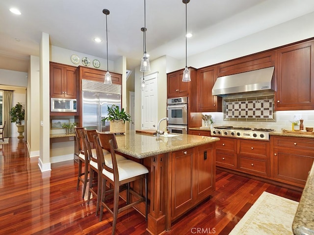 kitchen featuring built in appliances, dark hardwood / wood-style flooring, hanging light fixtures, and range hood