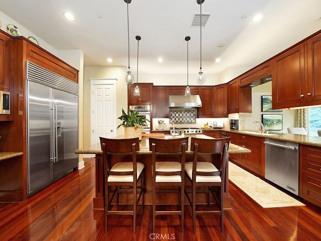 kitchen featuring dark wood-type flooring, hanging light fixtures, built in appliances, light stone countertops, and extractor fan