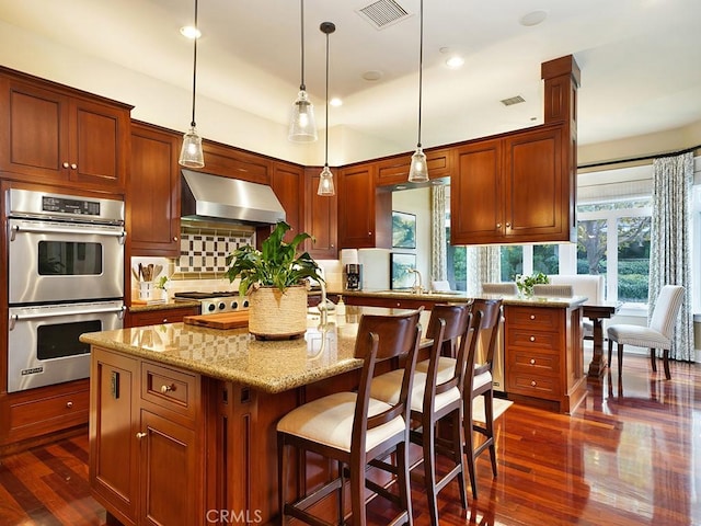 kitchen featuring decorative backsplash, appliances with stainless steel finishes, wall chimney exhaust hood, dark wood-type flooring, and a center island