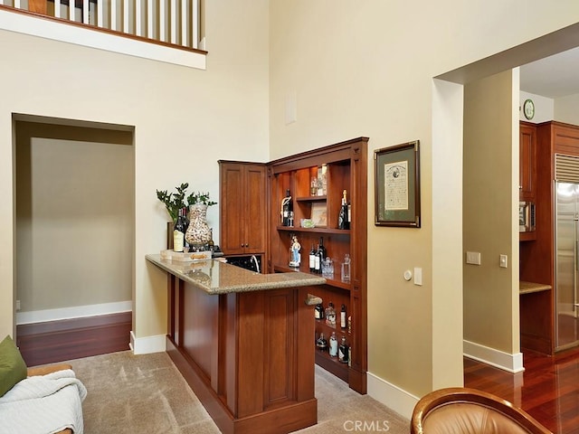 bar with built in refrigerator, light stone counters, dark hardwood / wood-style flooring, and a towering ceiling