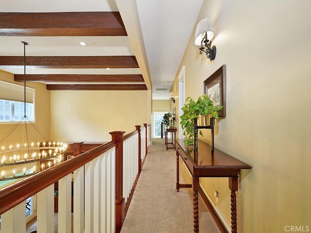 corridor with plenty of natural light, beamed ceiling, light colored carpet, and a notable chandelier