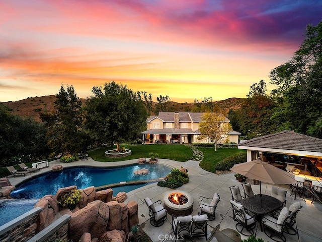 pool at dusk featuring a lawn, a patio area, and an outdoor fire pit