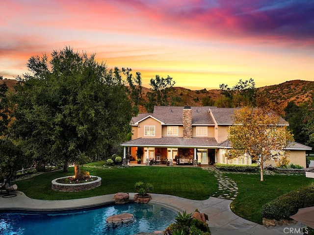 back house at dusk featuring a lawn and a mountain view