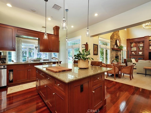 kitchen with sink, light stone counters, dark hardwood / wood-style flooring, pendant lighting, and a center island with sink