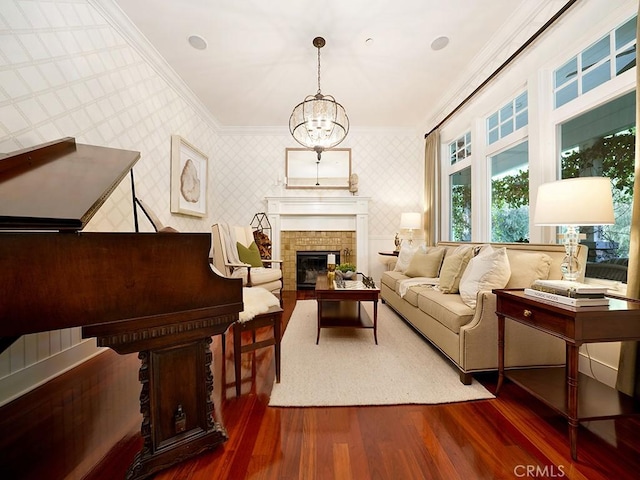 living area featuring an inviting chandelier, crown molding, dark wood-type flooring, and a brick fireplace