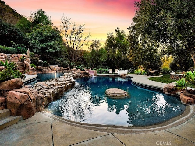 pool at dusk featuring pool water feature