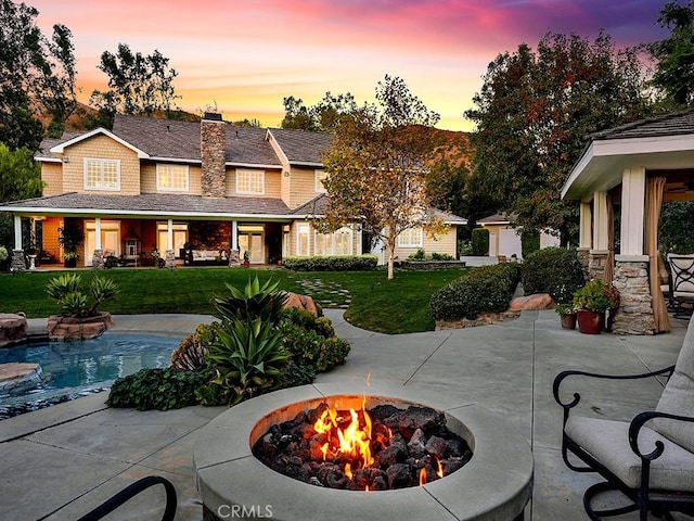 patio terrace at dusk featuring a lawn and an outdoor fire pit