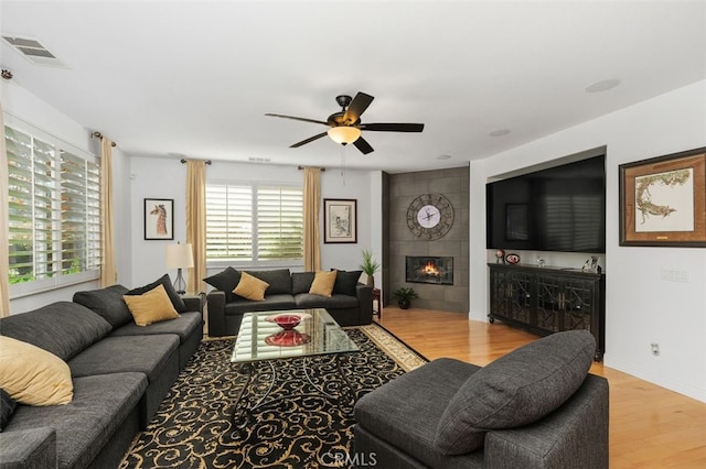 living room featuring a tile fireplace, light hardwood / wood-style flooring, and ceiling fan