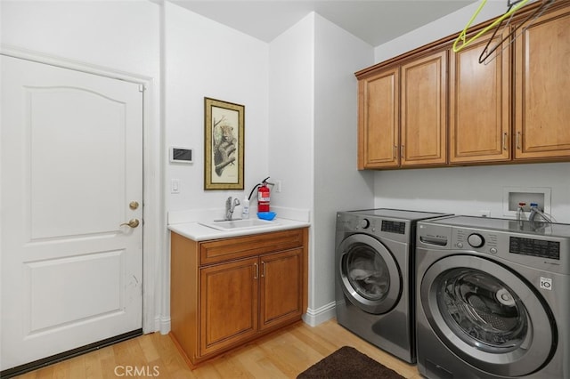 clothes washing area with washer and clothes dryer, cabinets, sink, and light hardwood / wood-style flooring