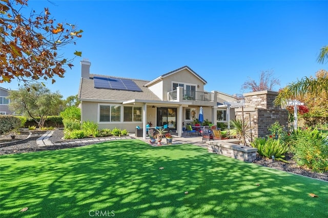 rear view of property featuring a lawn, solar panels, a balcony, and a patio