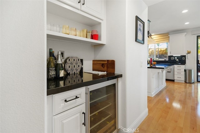 bar featuring decorative backsplash, stainless steel dishwasher, beverage cooler, light hardwood / wood-style flooring, and white cabinetry