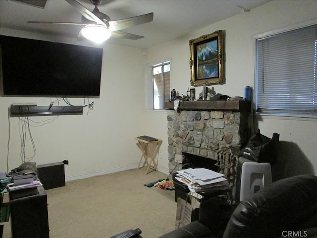 living room featuring carpet flooring, ceiling fan, and a stone fireplace