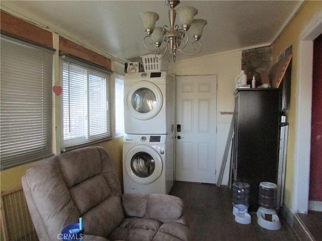 clothes washing area featuring stacked washer / drying machine, crown molding, and a chandelier