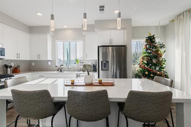 kitchen with white cabinetry, appliances with stainless steel finishes, decorative backsplash, a kitchen island, and sink